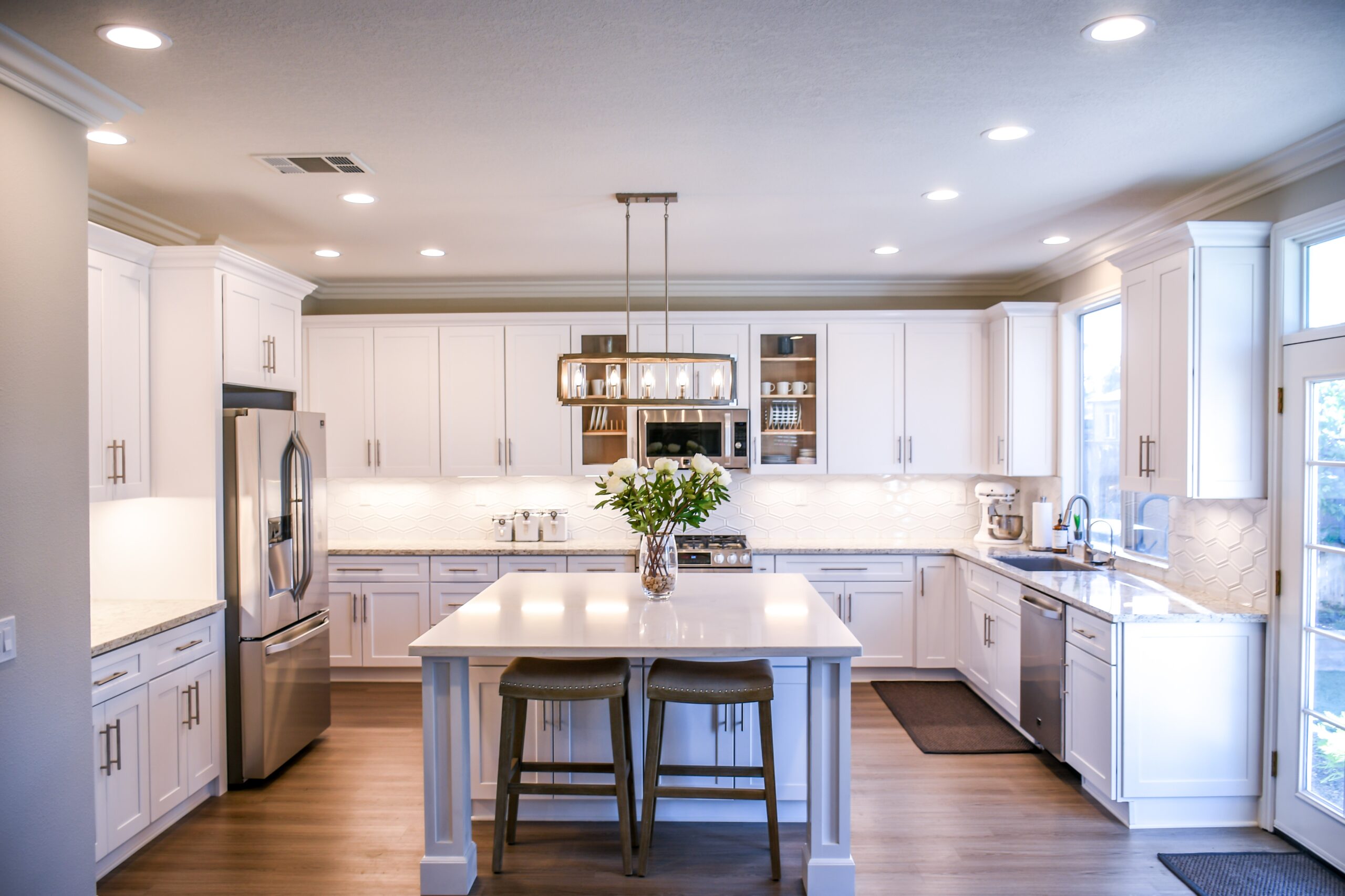 A kitchen with recessed electrical can lights, a modern island light fixture, and under cabinet lighting.